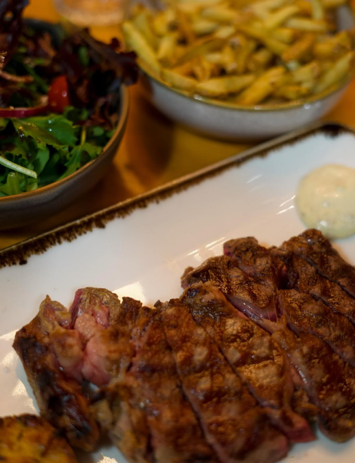 Bife fatiado e grelhado em um prato azul com osso, servido com molho.
