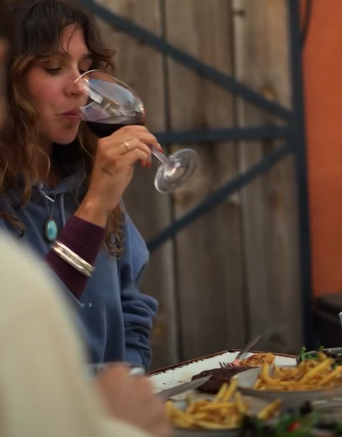 Mesa de jantar ao ar livre no terraço com bifes, hambúrgueres, bebidas e vista da cidade ao pôr do sol.