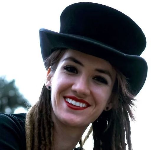 Smiling person in a black top hat with braided hair and red lipstick outdoors