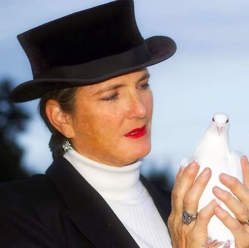 Woman in black hat holding a small white bird against a blurred outdoor sky background