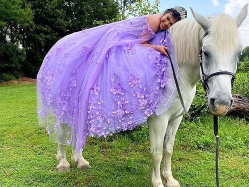 Person in a lavender gown leaning on a white horse in a grassy field