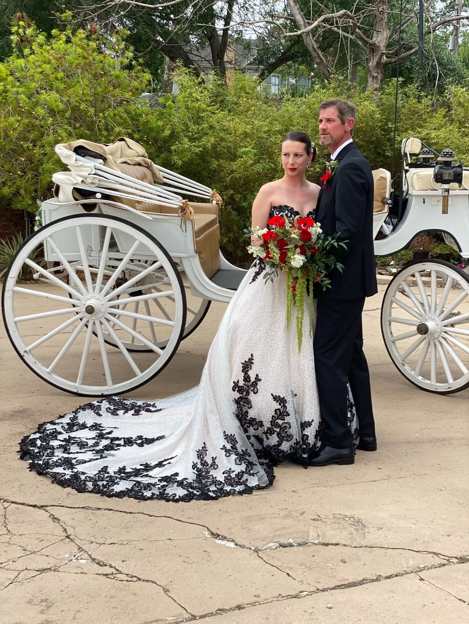 Bride and groom standing beside a white horse-drawn carriage, with a black-and-white wedding dress train.