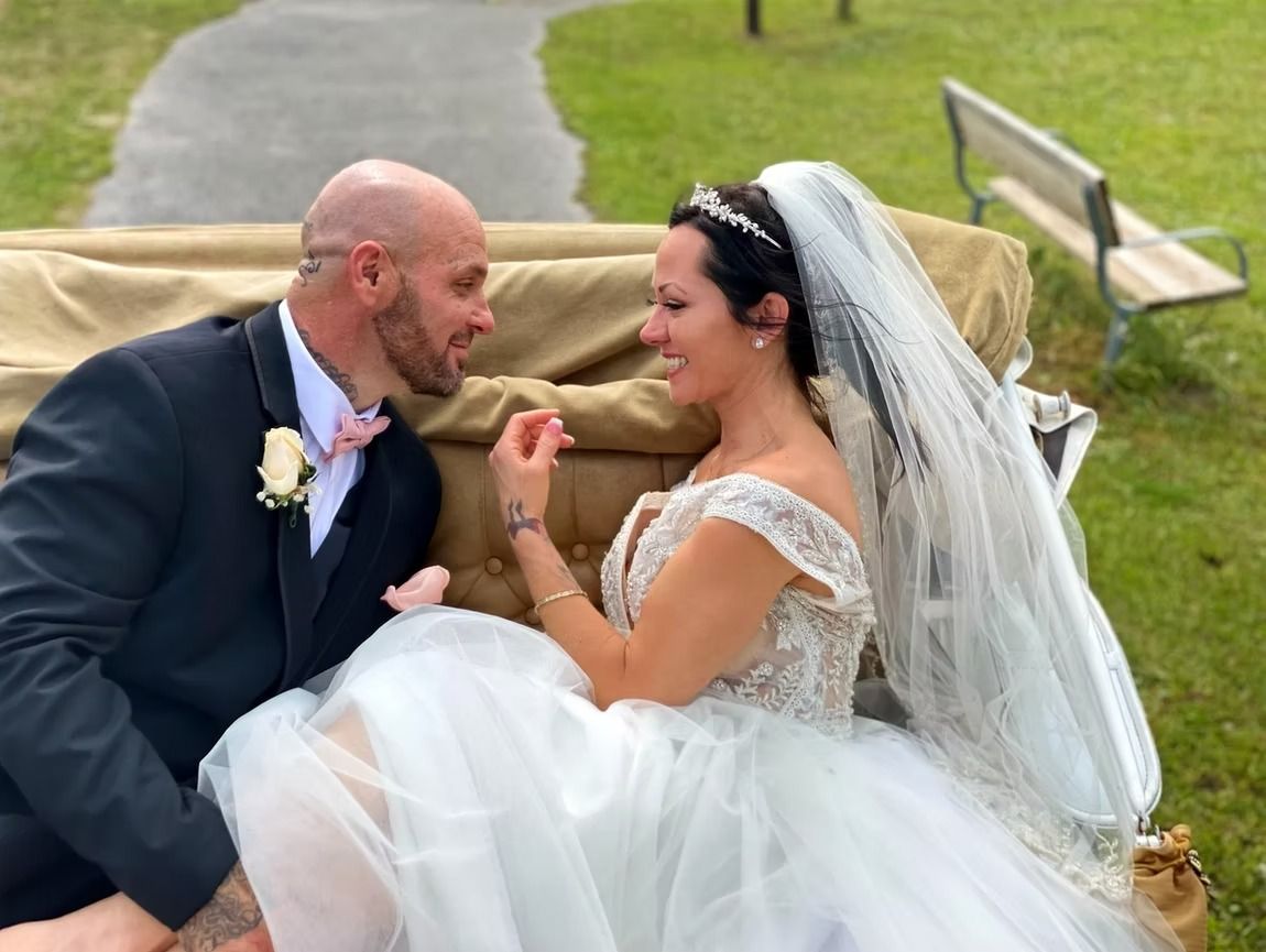 Bride and groom in wedding attire sharing a kiss outdoors on a grassy path