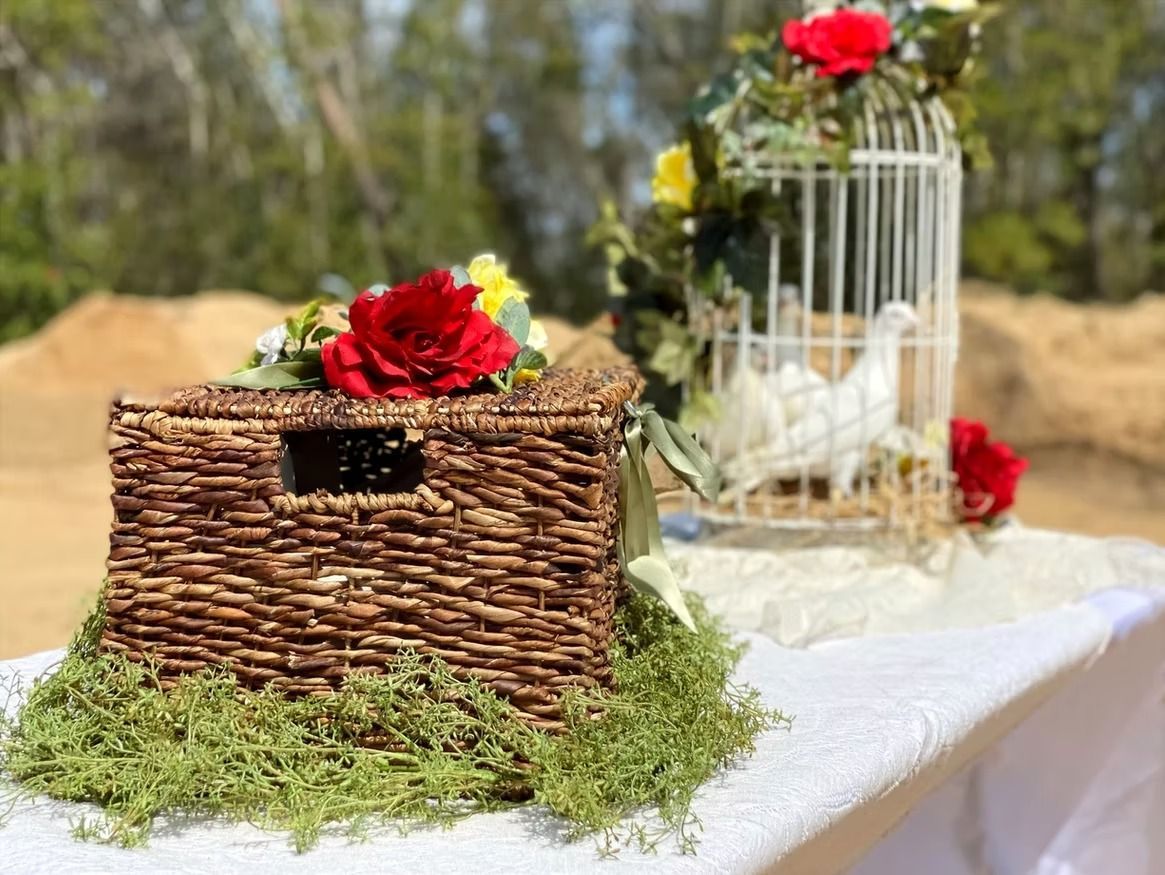 Rustic woven basket and white birdcage decorated with red roses on a table outdoors