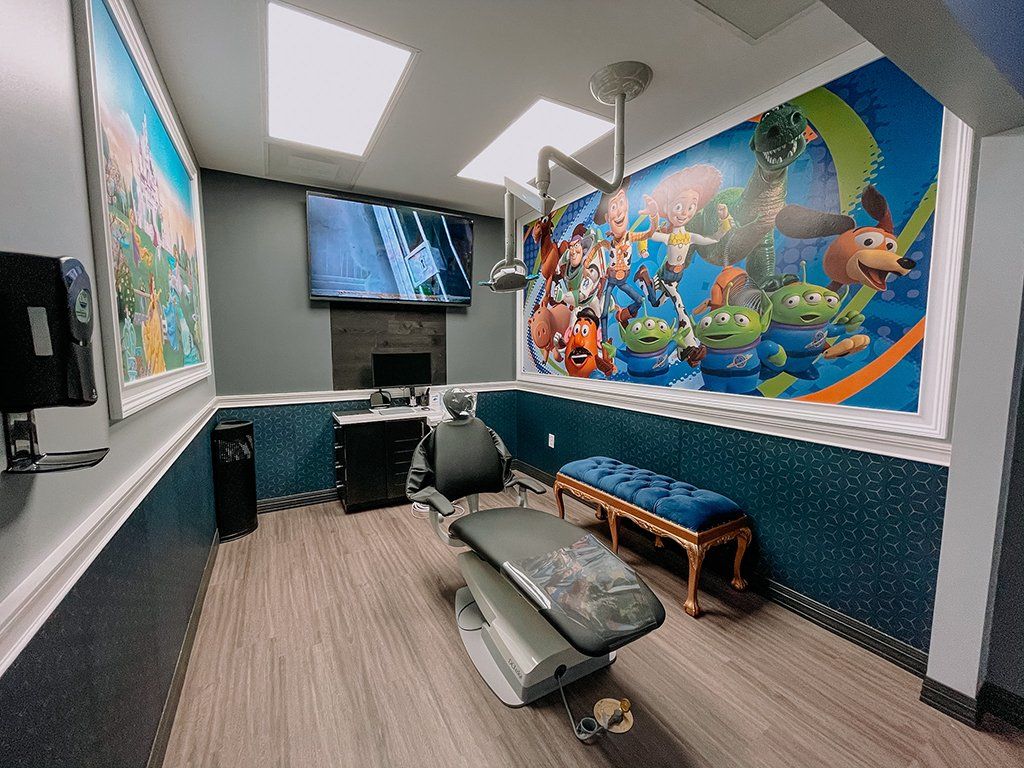 Dental office room with a patient chair, Toy Story mural, TV, and blue accents.