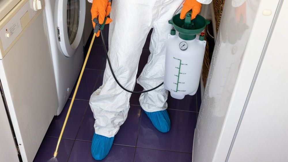 A person in a protective suit is spraying a room with a sprayer.