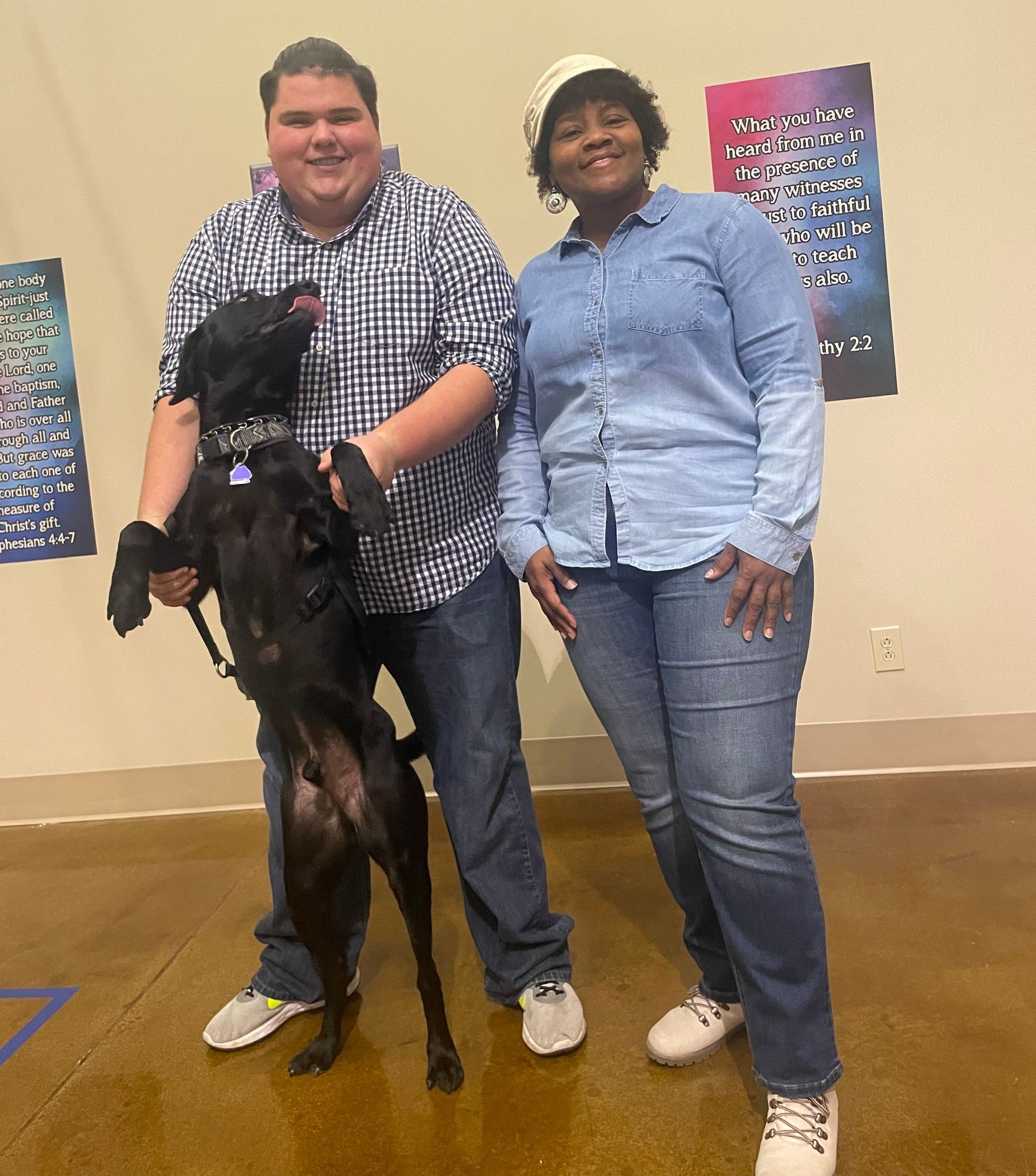 A man and a woman are standing next to a black dog.