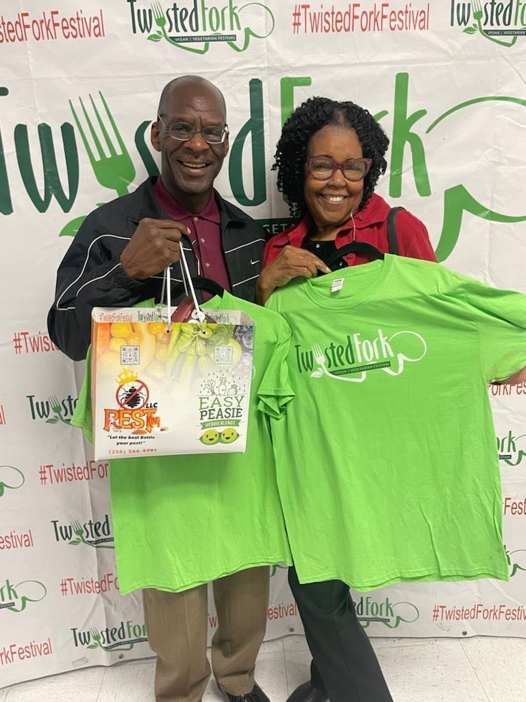 A man and a woman are holding green t-shirts and a bag.