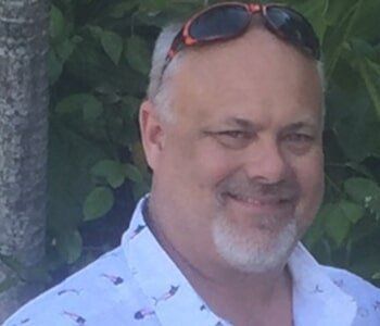 A man with a beard is wearing sunglasses and a white shirt.