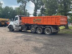 An orange dump truck is parked in a gravel lot.