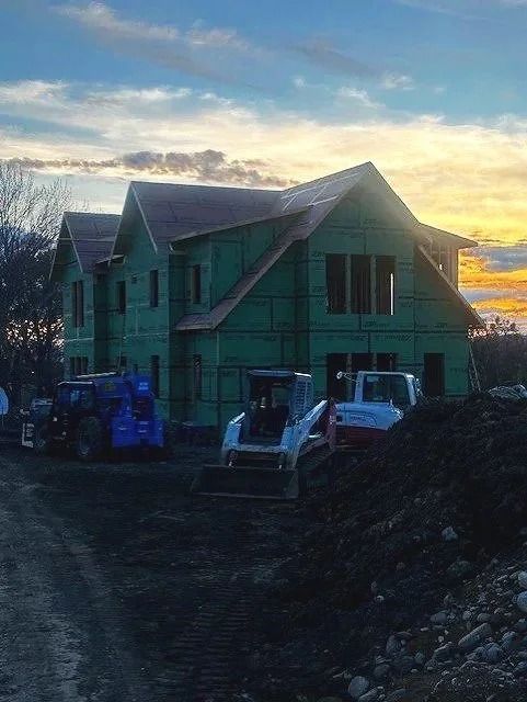 Partially built green house at sunset with construction equipment in front