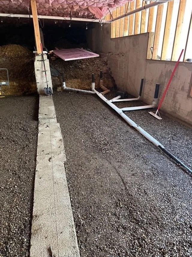 Gravel-covered basement with a concrete center strip, white pipes, and exposed wooden framing.