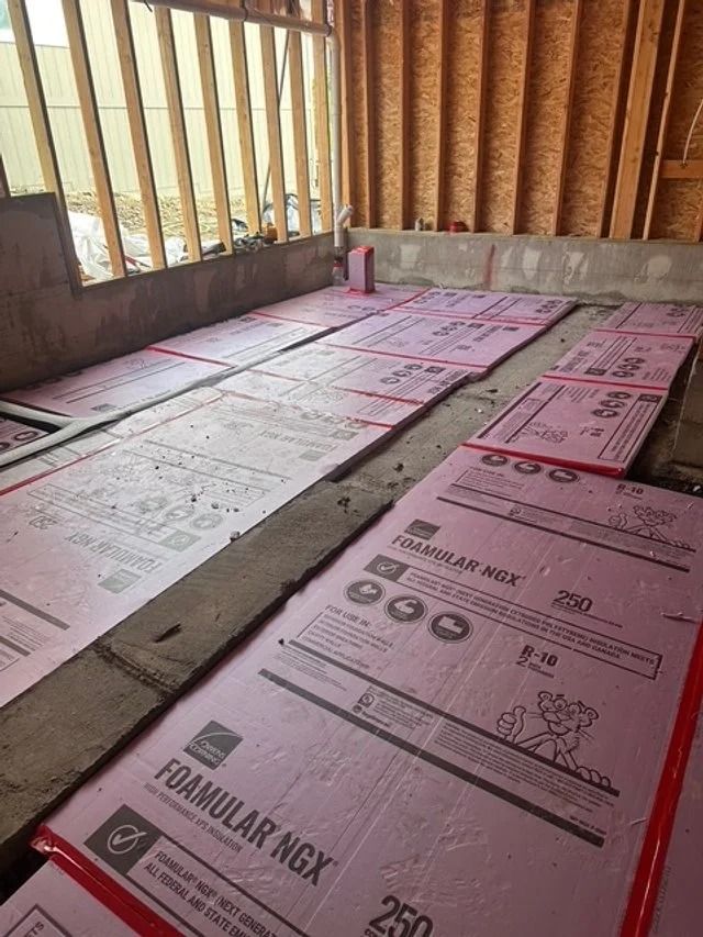 Insulated foam boards laid on a floor inside a room with unfinished wooden walls and windows