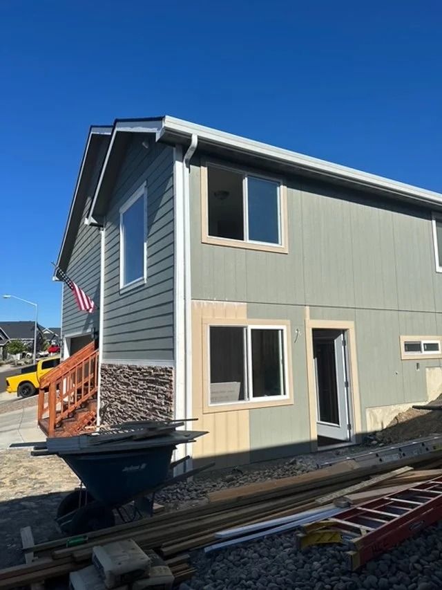 Two-story gray house with tan trim, side stairway, and American flag under a clear blue sky. Two-story gray house with tan trim, side stairway, and American flag under a clear blue sky.
