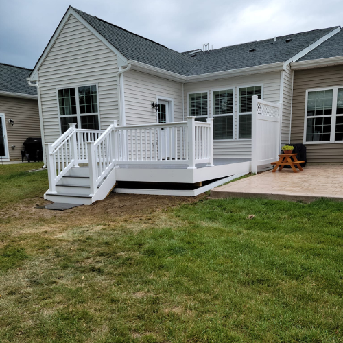A white deck with stairs and a picnic table in front of a house.
