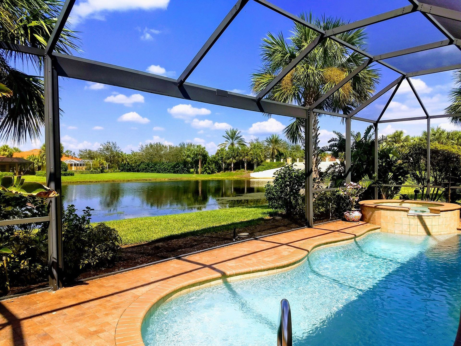 A large swimming pool is surrounded by a screened in area with a view of a lake.