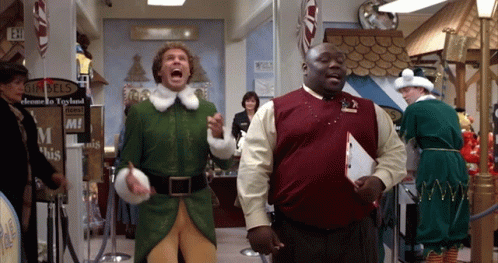 Buddy the Elf excitedly running with a mall employee in a holiday store.