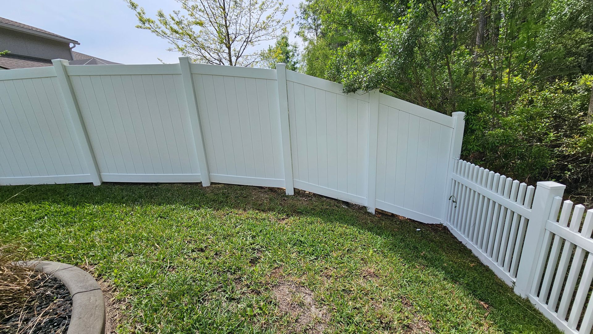 White vinyl fence surrounding a grassy backyard, with a picket fence section on the right.