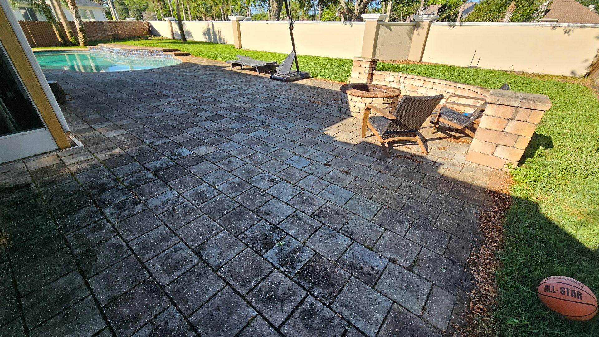 Patio with brick pavers, pool, fire pit, chairs, and lawn. Sunny outdoor scene.