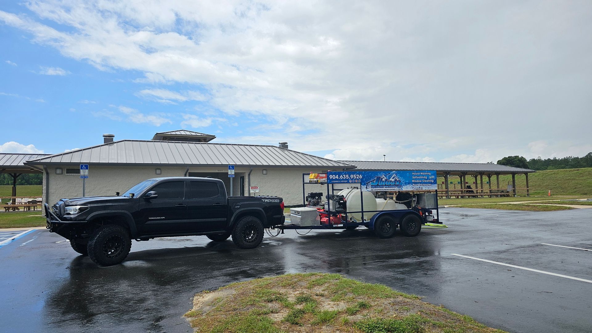 Black truck towing a trailer parked near a building on a wet day.