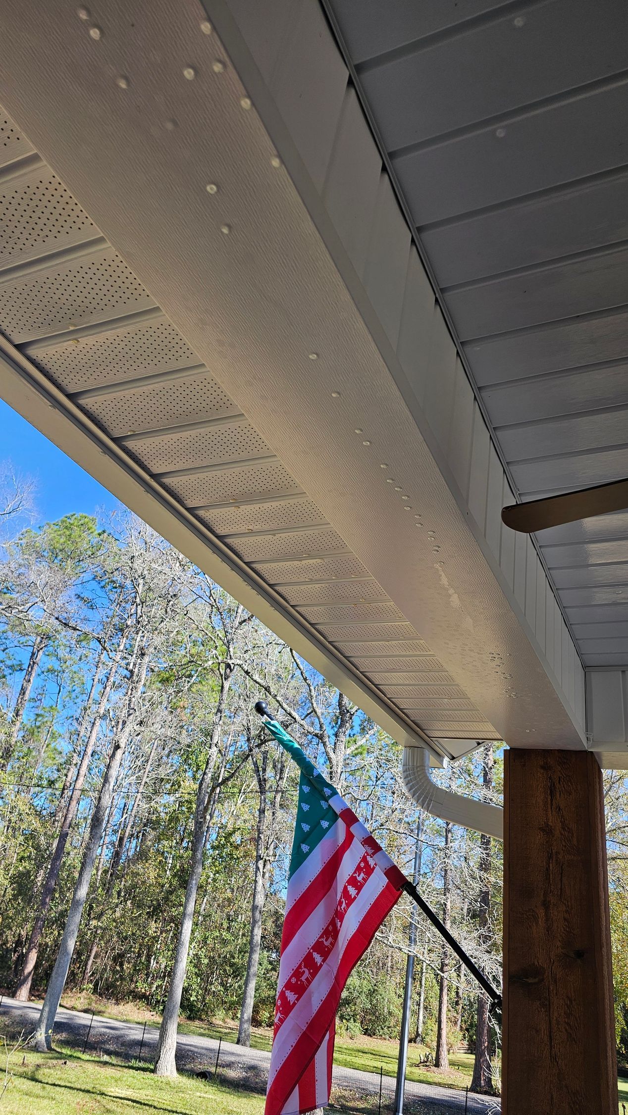 View from under a porch with an American flag and trees in the background.