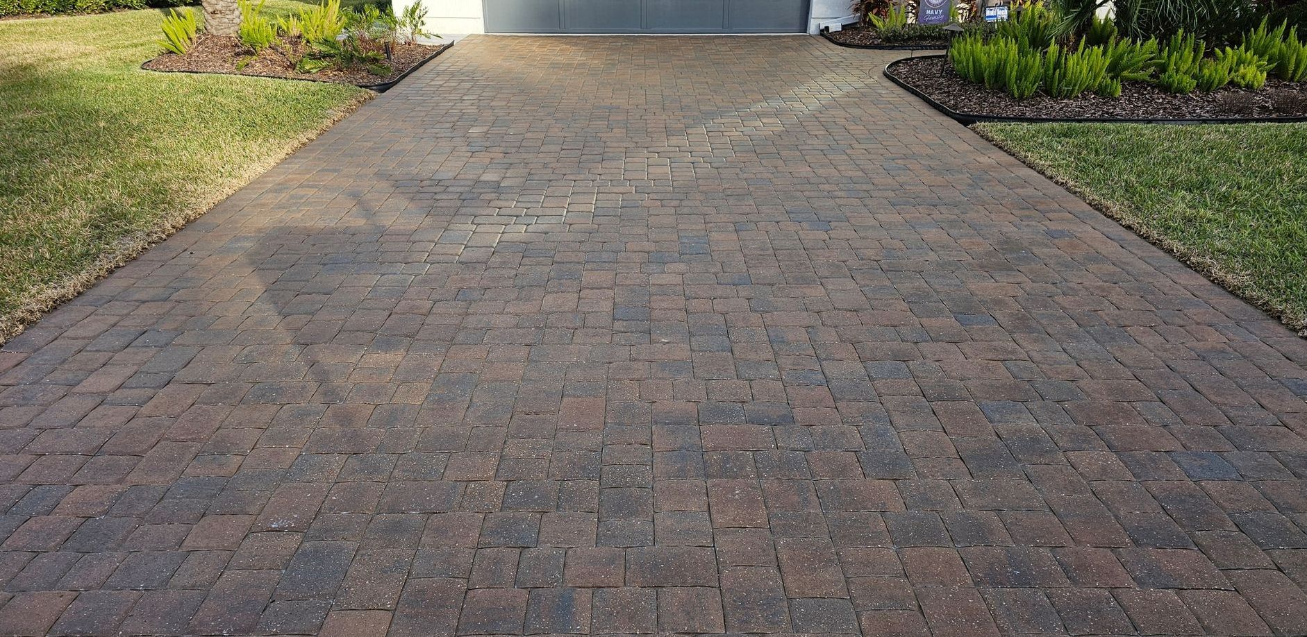 A brick driveway with a sidewalk in front of a house.