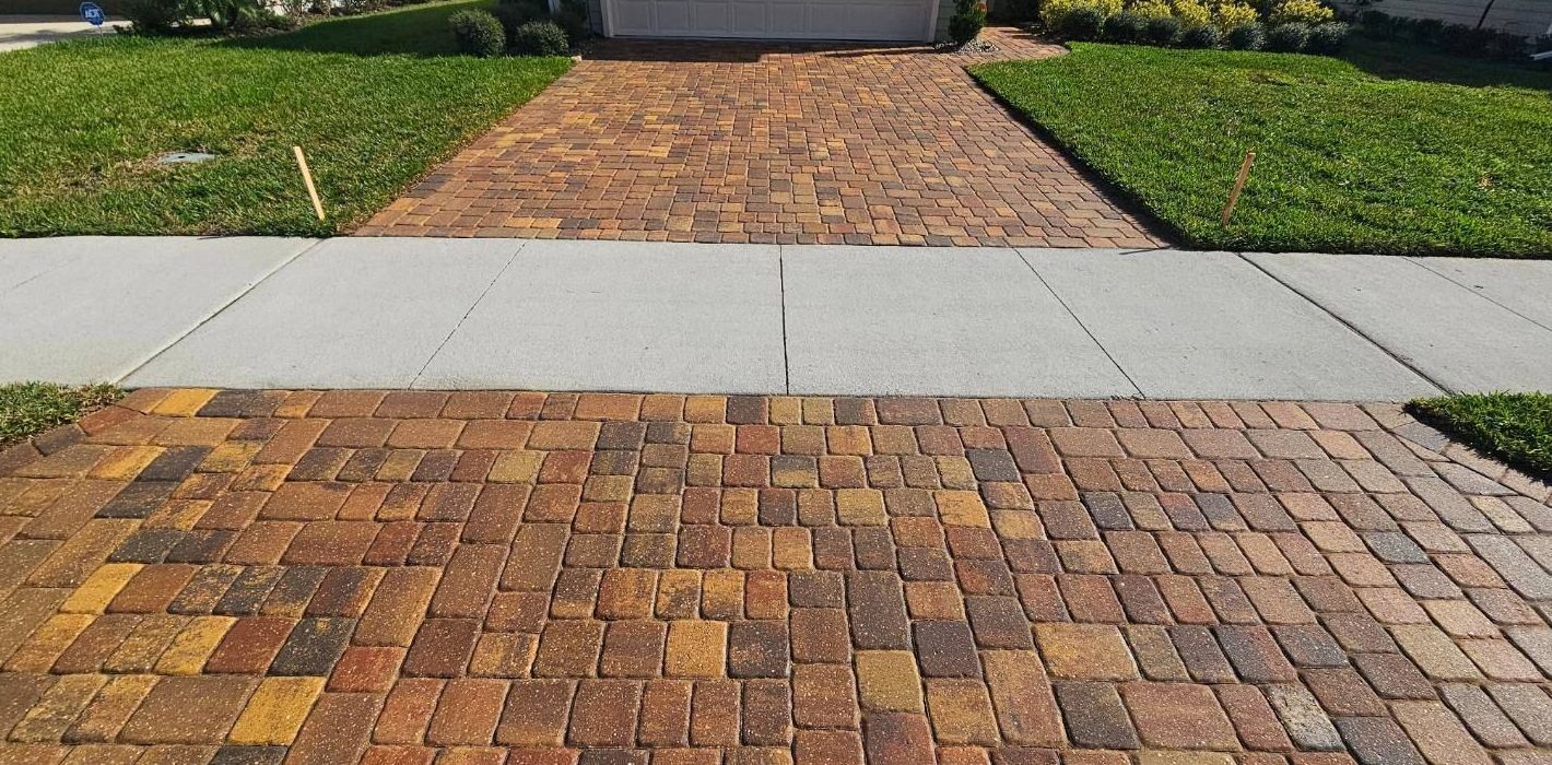 A brick driveway with a sidewalk in front of a house.