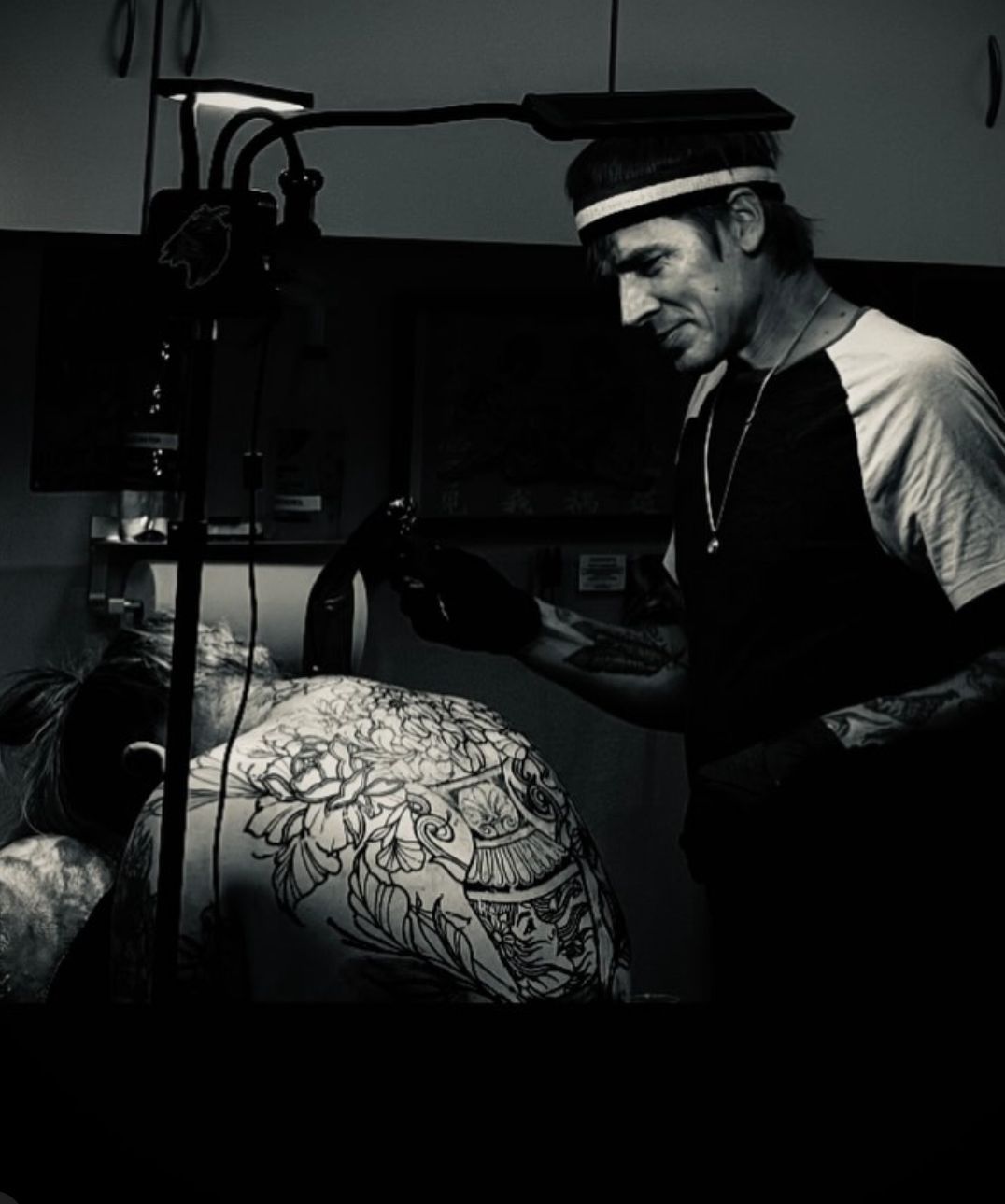 Artist working on a tattoo design beside a torso sketch in a dim studio