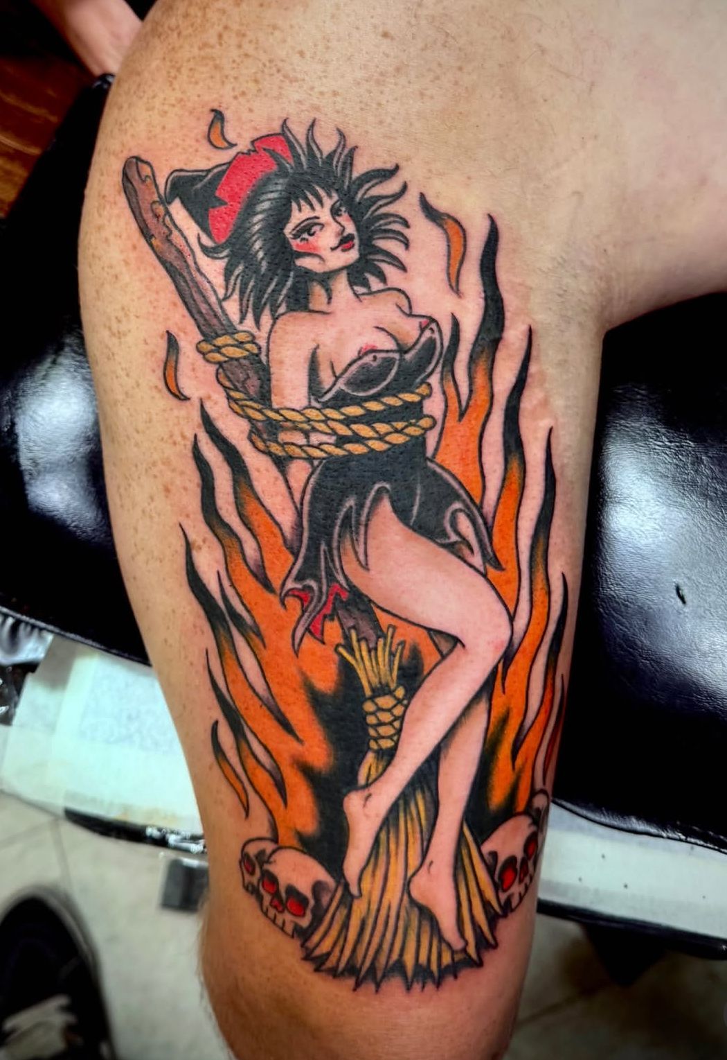 Demonic pin-up tattoo in black and red, with flames, a sword, and a small skull on skin