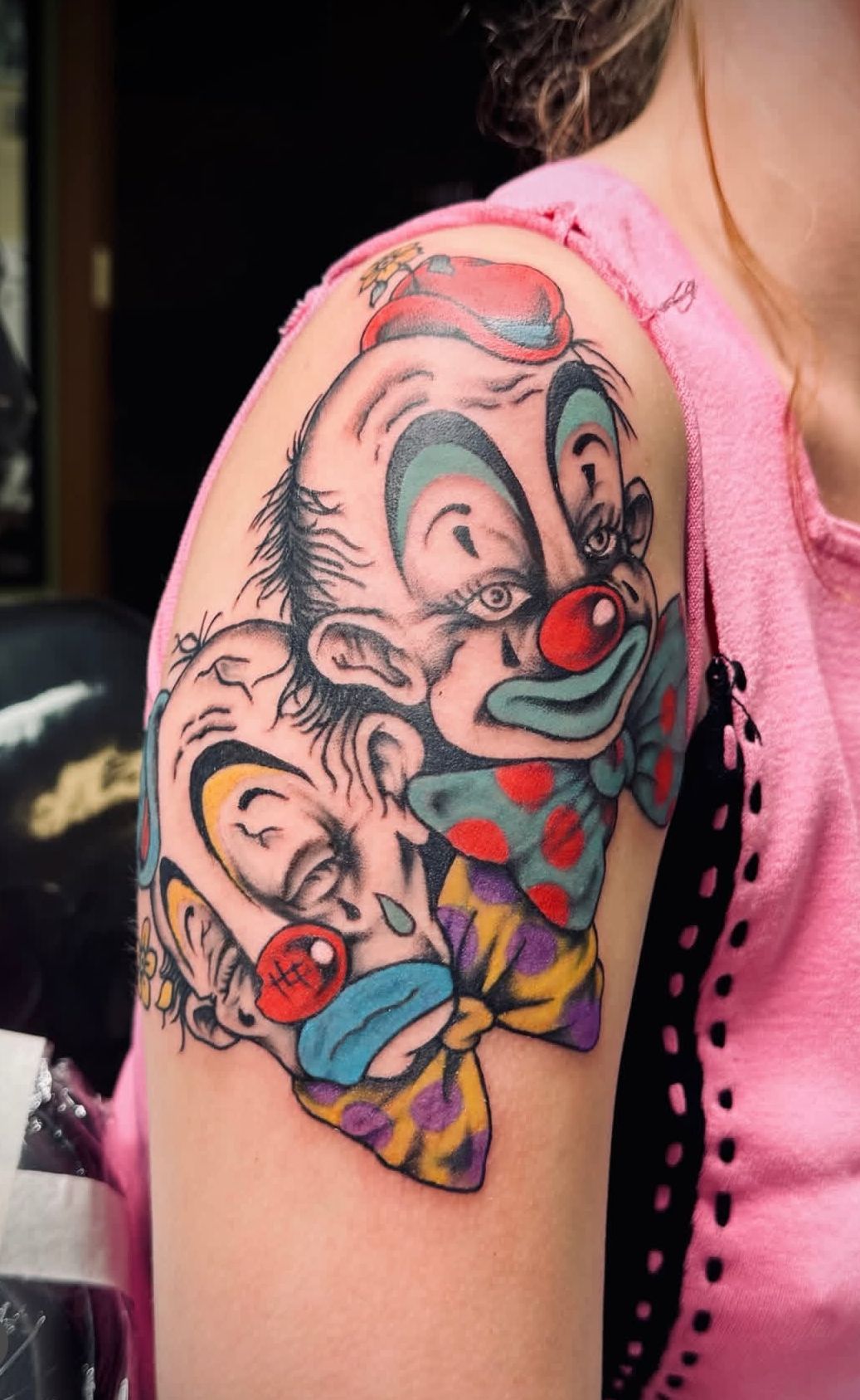 Colorful clown face tattoo on upper arm with red nose and pink shirt sleeve