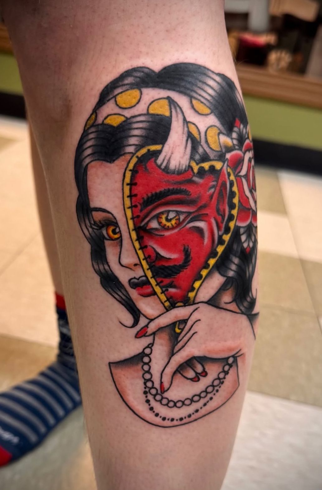 Colorful tattoo of a woman’s face split down the middle, with one side red and one side natural, on a leg