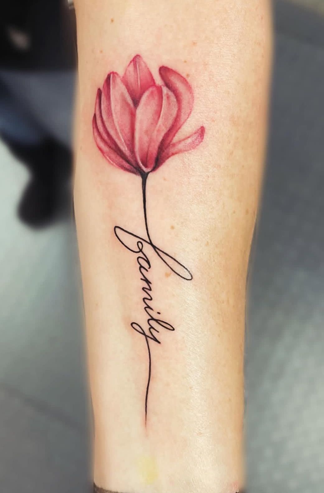 Pink flower tattoo with the word “family” on a forearm