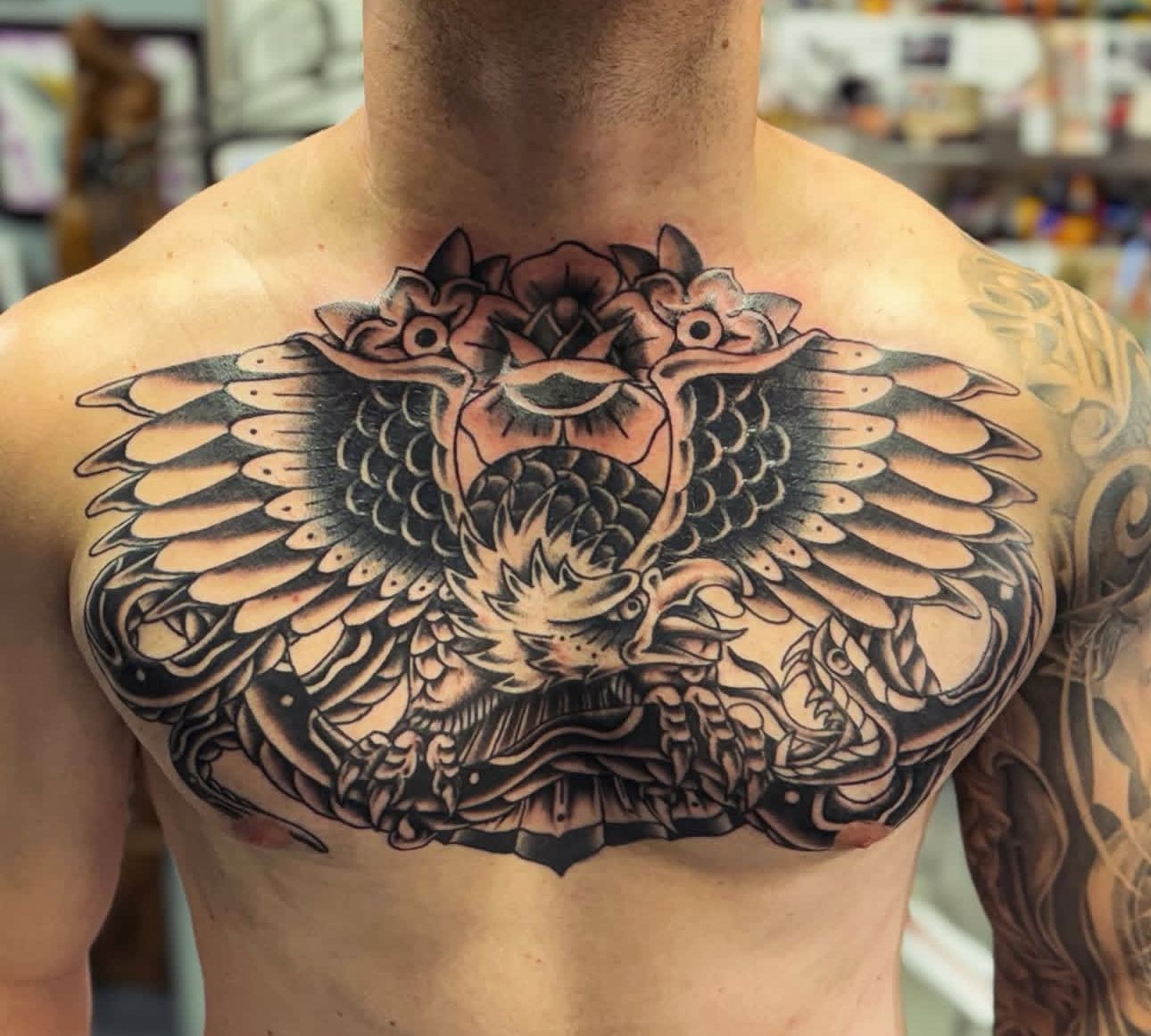Chest tattoo of a detailed black-and-gray owl with outstretched wings and flowers on an upper torso