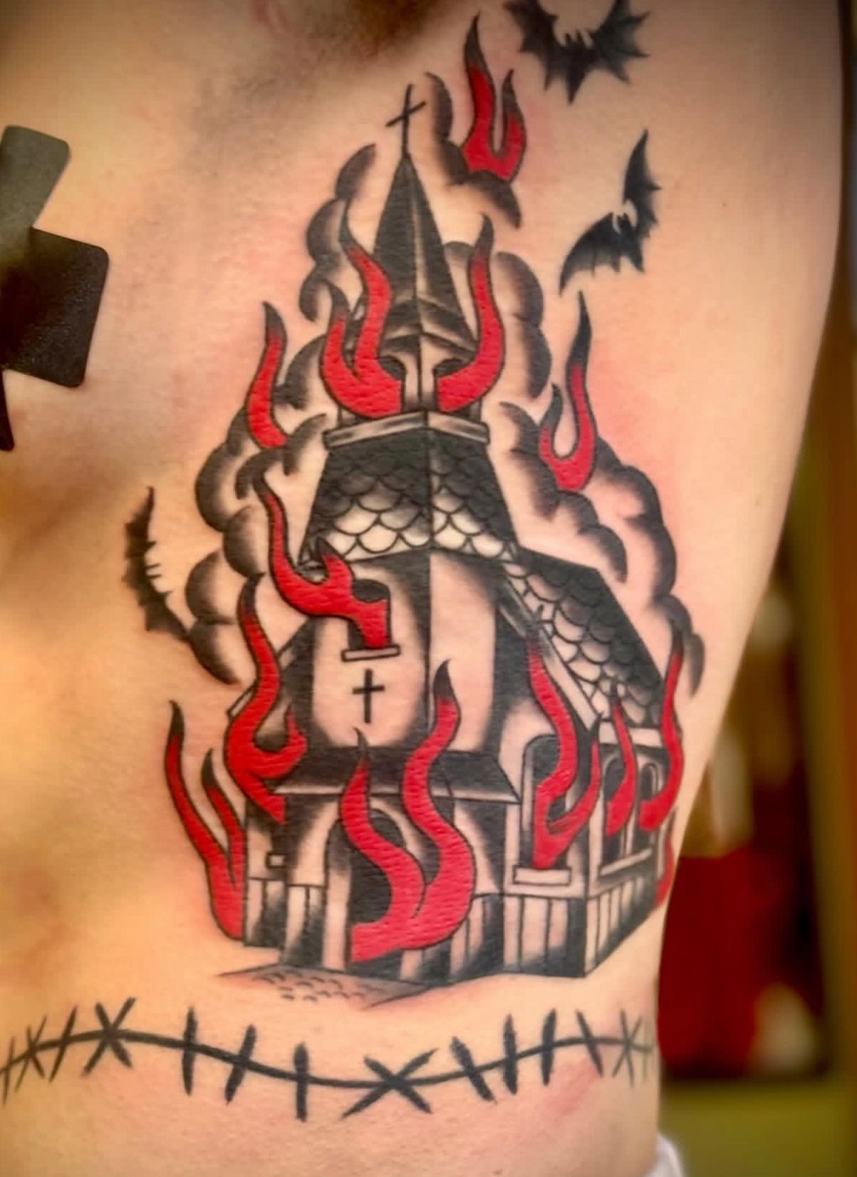 Black-and-red tattoo of a gothic church with flames and a cross on a person’s skin