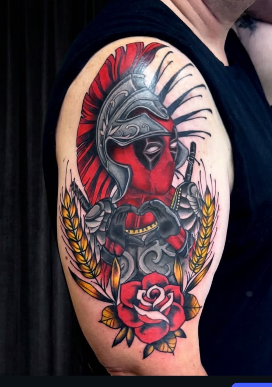 Arm tattoo of a red-faced warrior in a silver helmet with laurel leaves and a pink rose under a black sleeve