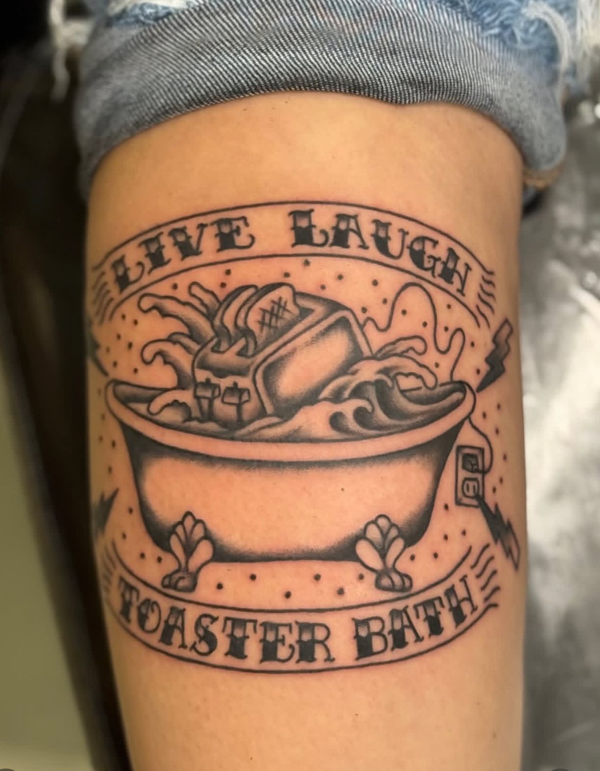 Arm tattoo of a toaster bath with banner text “LIVE LAUGH TOASTER BATH.”