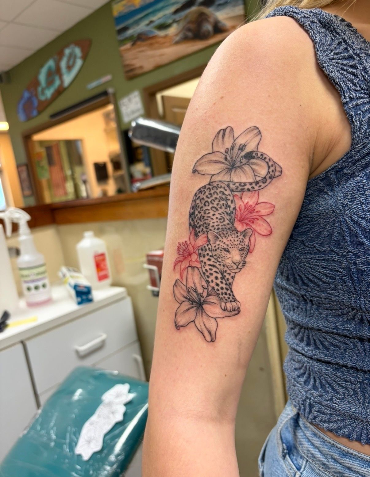 Upper arm tattoo of flowers and a snake on a person wearing a blue sleeveless top