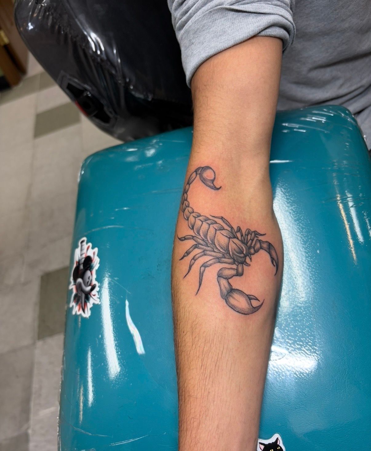 Arm with scorpion tattoo resting on a teal chair