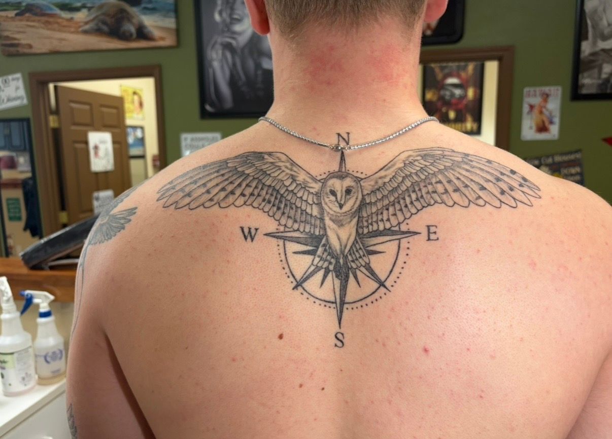 Back of a person showing a black winged compass tattoo across the upper shoulders