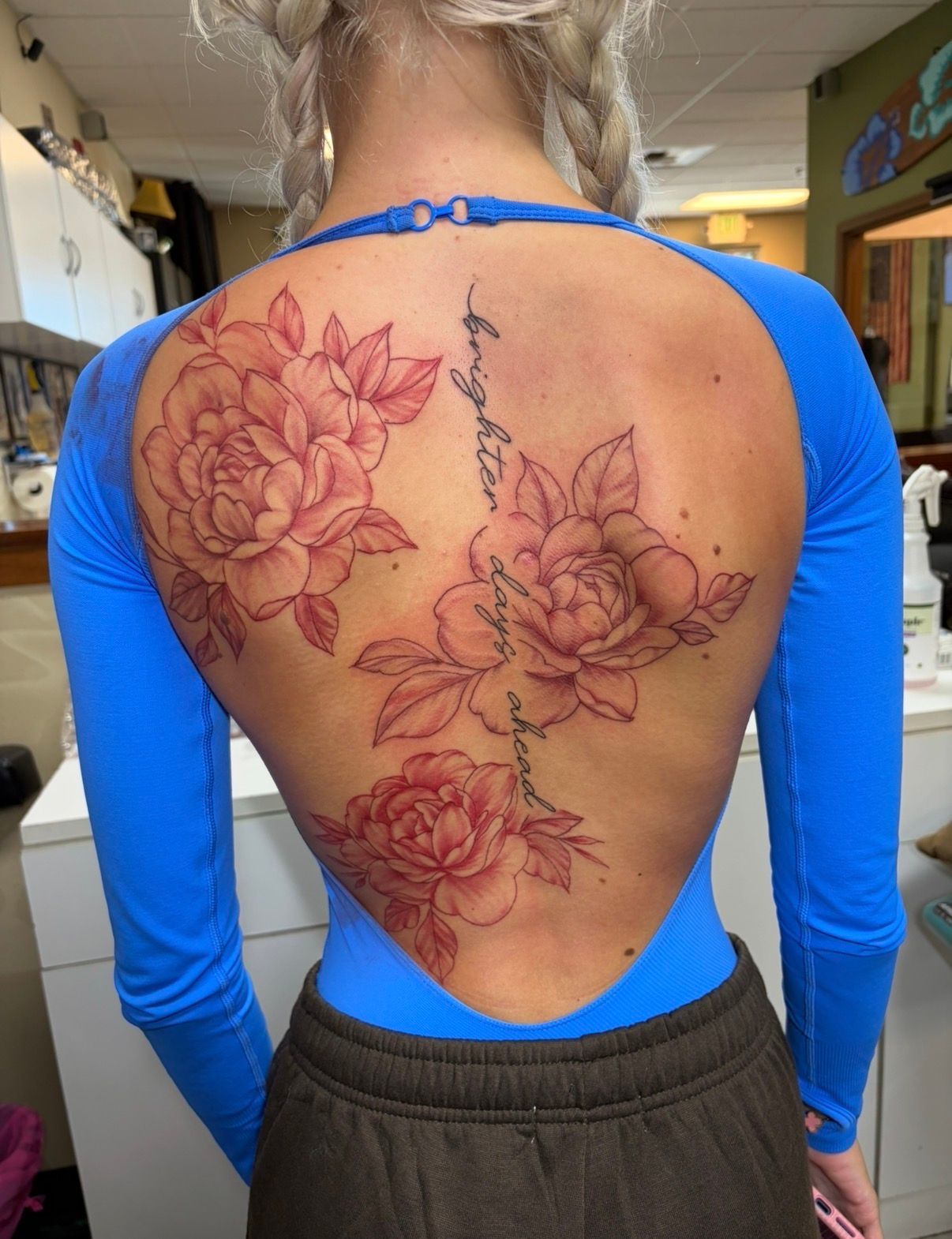 Woman’s back with a large floral spine tattoo in red linework, wearing a bright blue open-back top