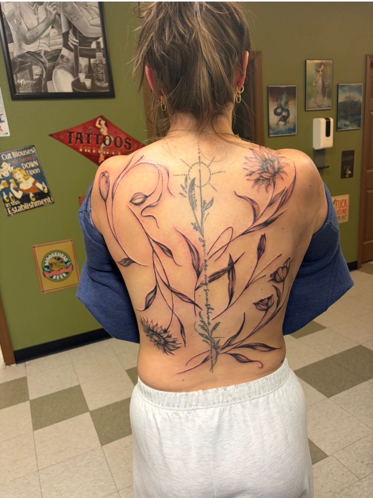 Person with floral back tattoo standing indoors in a green-walled room.