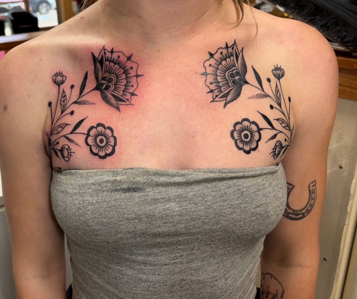 Upper chest with symmetrical black floral tattoos above a gray tube top