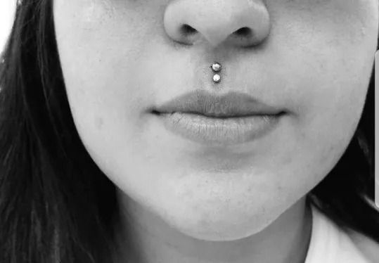 Close-up of a face with a septum piercing and neutral expression in black and white.