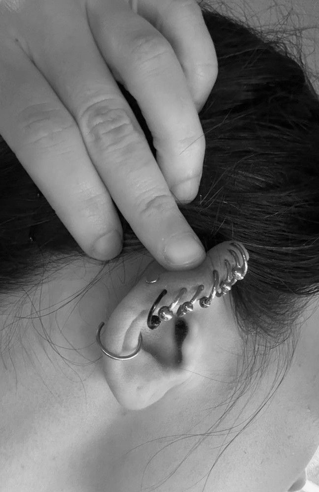 Hand adjusting a silver ear cuff on a person’s ear, close-up black-and-white shot