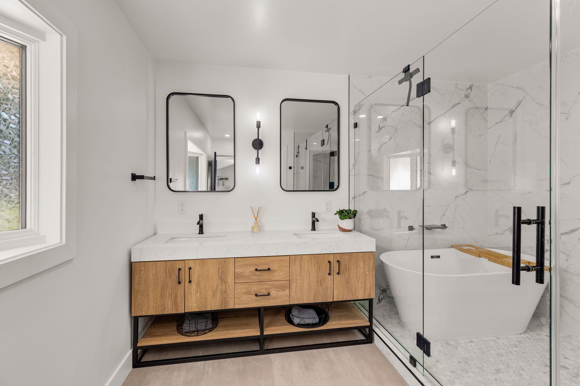 Modern white bathroom with wood vanity, double mirrors, bathtub, and glass shower.
