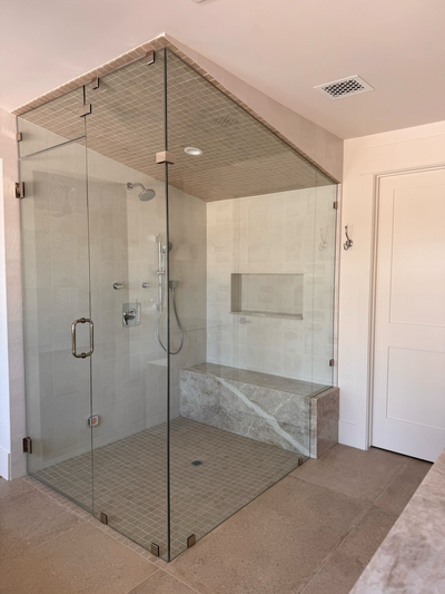 Glass shower enclosure in a bathroom with marble bench and tiled floor.