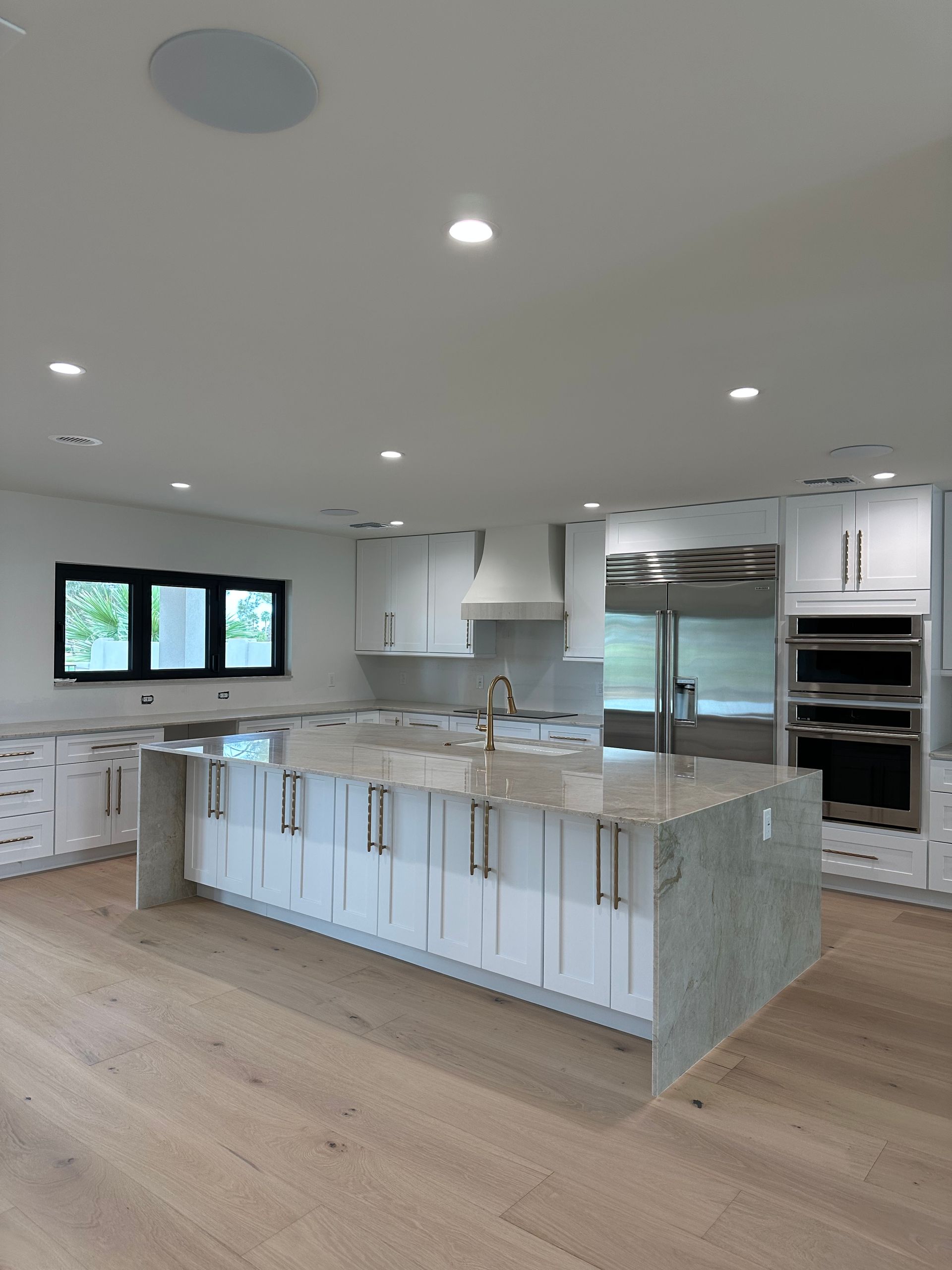 Bright modern kitchen with white cabinets, marble island, stainless appliances, and wood floors in Goodyear, AZ by Botello Builders