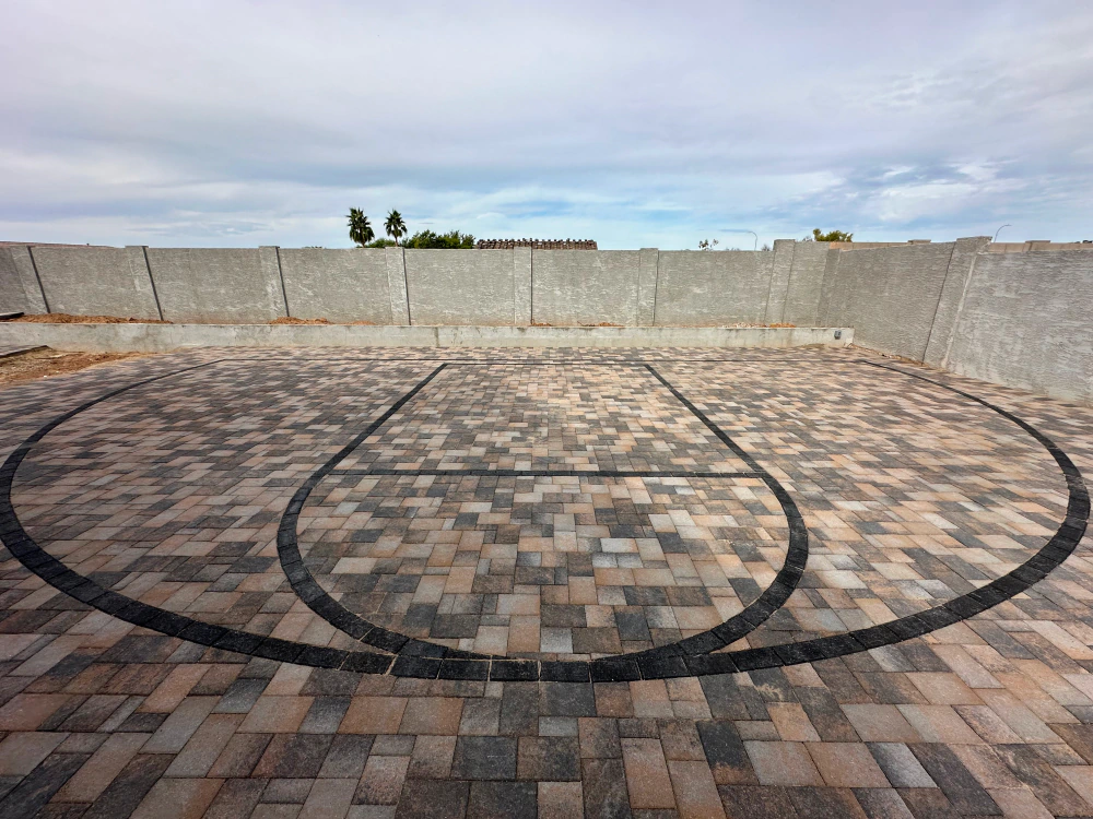 Outdoor brick plaza with a circular mosaic pattern and concrete wall under a cloudy sky