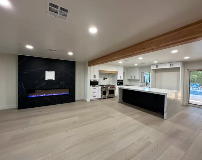 Modern open-concept living room and kitchen with fireplace, island, light wood floors, and recessed lighting