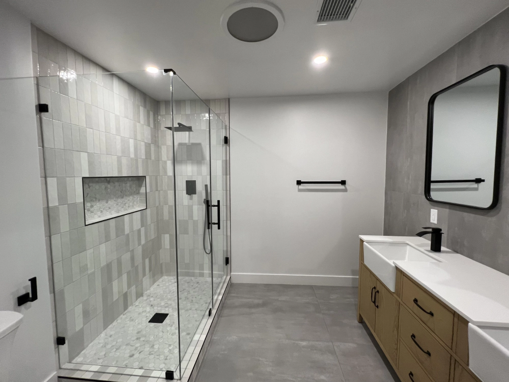 Modern bathroom with walk-in glass shower, gray tile, and white vanity with mirror.